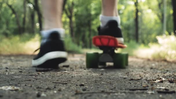 サマーパークでは 男性の足のクローズアップがボードに乗り始めます 屋外の公園でスケートボードに乗るスケーターの少年 オレンジスケートフットウェアシューズ スケートボードデッキ — ストック動画