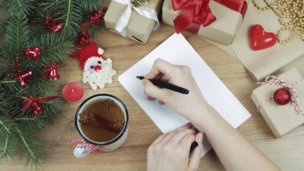 女性の手は彼女の未来を計画し 白い紙のシートにリストを行うために新年を書いています モミの枝 贈り物とクリスマスの装飾 平置きだ最上階だモックアップ テキストのコピースペース — ストック動画