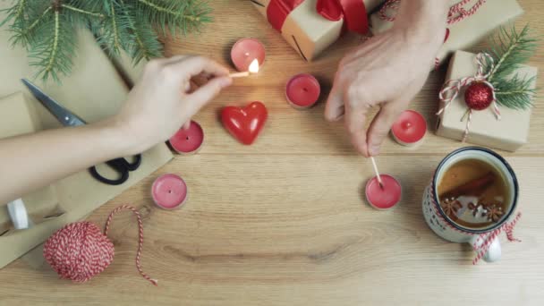 木製のテーブルの上にギフトボックスのフラットレイシーンビデオ テーブルの上に美しい装飾品とお茶のカップと松の枝 男と女の誰かがキャンドルを点灯し クリスマスフェスティバルのコンセプト — ストック動画