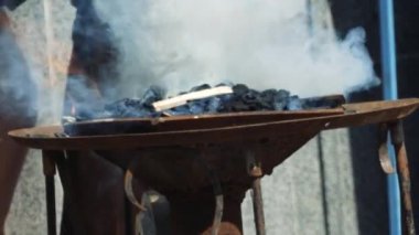 Demirci metal dövme için bir fırın hazırlar. Demirci fırına kömür döküyor.