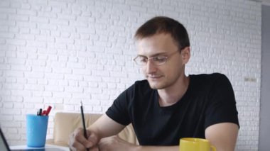 Dizüstü bilgisayara yazı yazan genç beyaz adamın portresi konsantre saatler ve evde kameraya gülümsüyor. Kavram serbest çalışma, iş, iletişim, eğitim. 