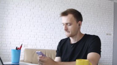 Genç yakışıklı beyaz adam evde kulaklık bilgisayarda müzik dinliyor. 