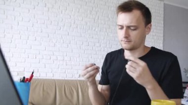 Genç yakışıklı beyaz adam kulaklıkla bilgisayardan müzik dinliyor ve evde çalışıyor. Serbest veya eğitim konsepti.