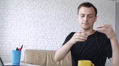 Genç yakışıklı neşeli beyaz adam kulaklık la bilgisayarda müzik dinlerken ve evde çalışıyor. Serbest veya eğitim konsepti.
