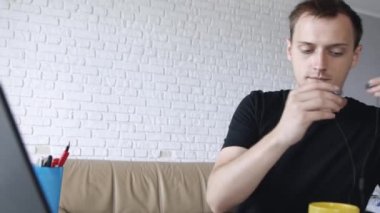 Genç yakışıklı neşeli beyaz adam kulaklık la bilgisayarda müzik dinlerken ve evde çalışıyor. Serbest veya eğitim konsepti.