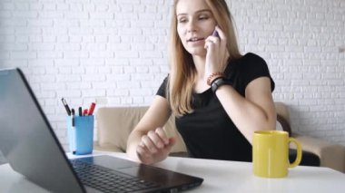 Ev-ofis kapalı dizüstü kullanırken bir telefon görüşmesi olan mutlu genç beyaz kadın yakın çekim. Kavram iş, iletişim, eğitim.