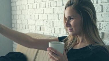 Güzel genç beyaz kadın sabah kahve içiyor ve televizyon izliyor. Yakın çekim portre.