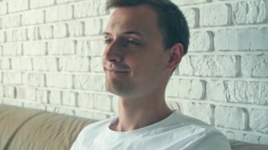 Çekici genç Beyaz adam kahve içiyor, sabah ları televizyon izlerken gülüyor. Yakın çekim portre.