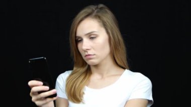 Genç beyaz kadın telefon ekranına bakarak konsantre oldu. Portreyi kapat. Siyah arka planda duran kayıtsız kadın. 