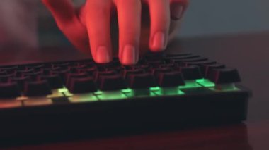 Genç oyuncu bir video oyunu oynar, ellerin yakın çekim, oyuncu oyun klavyesi kullanır, ışıklı mercan rengi ve çok renkli neon, cybersportsman.