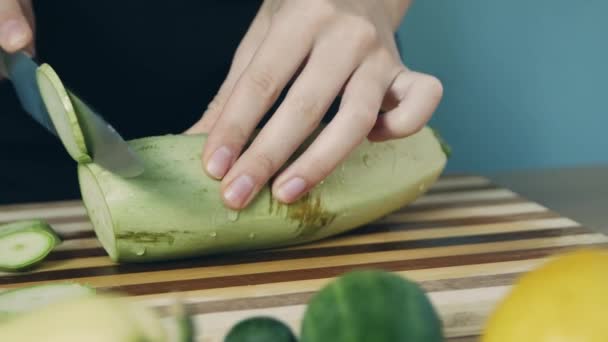 キッチンで木製のボードのスライスに緑のズッキーニをカット若い女性 クローズアップ ズッキーニの指輪 サラダに野菜を切る 健康食品 — ストック動画