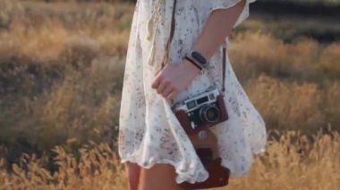 Beyaz elbise genç güzel kadın bir gün batımı arka planda eski retro kamera ile alan yürüyüş. Doğa yavaş hareket videosu. Kapat şunu. Alanında doğa ve güneş ışığına sahip Carefree kadın. 