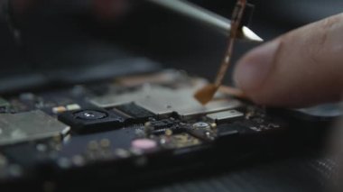 Cep telefonu tamir sürecini gösteren yakın çekim. Tamircinin elleri tornavidayla vidaları çıkarıyor. Akıllı telefonun dahili bileşenleri. Sökülmüş cep telefonu. 