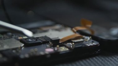 Cep telefonu tamir sürecini gösteren yakın çekim. Tamircinin elleri tornavidayla vidaları çıkarıyor. Akıllı telefonun dahili bileşenleri. Sökülmüş cep telefonu. 