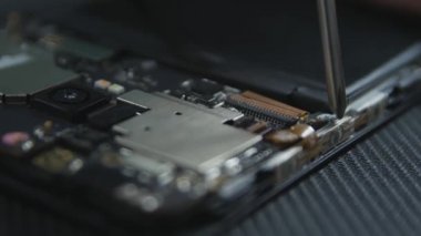 Cep telefonu tamir sürecini gösteren yakın çekim. Tamircinin elleri tornavidayla vidaları çıkarıyor. Akıllı telefonun dahili bileşenleri. Sökülmüş cep telefonu. 