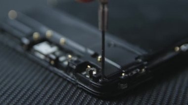 Cep telefonu tamir sürecini gösteren yakın çekim. Tamircinin elleri tornavidayla vidaları çıkarıyor. Akıllı telefonun dahili bileşenleri. Sökülmüş cep telefonu. Kopyalama alanı.