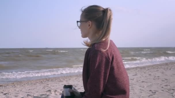 海辺でコーヒーや紅茶を飲む白人女性のサイドビュークローズアップ 彼女はビーチでくつろいでいる 髪に風 — ストック動画
