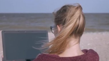 Genç, yakışıklı kadın güneşin batarken sahilde bir dizüstü bilgisayar üzerinde çalışıyor. Genç işadamı gün batımında bir deniz plajında çalışıyor. Bir serbest deniz kıyısında çalışır.