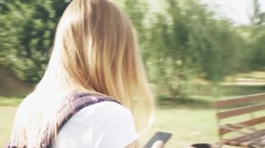 Gözlüklü gülümseyen beyaz bir kadın şehir parkında yürür ve telefonunu kullanır. Beyaz t-kısa Pretty yaz kadın onun cep telefonu bakarak sokakta yürür