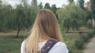 Gözlüklü gülümseyen beyaz bir kadın şehir parkında yürür ve telefonunu kullanır. Beyaz t-kısa Pretty yaz kadın onun cep telefonu bakarak sokakta yürür