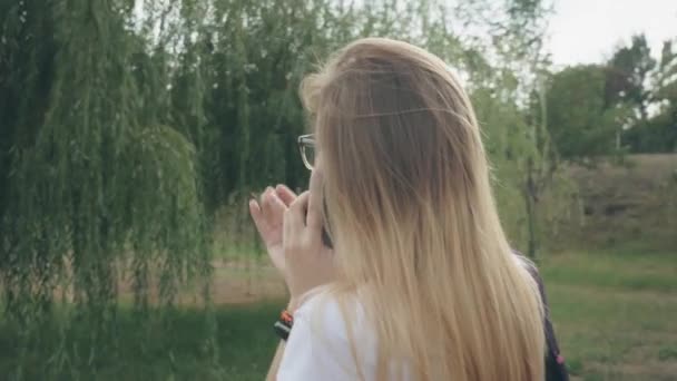 Femme heureuse dans des lunettes parlant sur téléphone portable, à l'extérieur. Une caucasienne parlant au téléphone marchant dans le parc. Attrayant jeune femme parlant sur téléphone portable tout en marchant dans le parc .