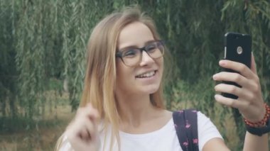 Gözlüklü beyaz renkli genç kız, açık havada yazlık parkta görüntülü görüşme yaparken kameradaki erkek arkadaşına ekrana el sallıyor. Mutlu kadın video çeviri aboneleri ile görüşmeler. 