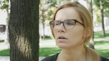 Gözlüklü genç beyaz kadın alerjisi olan parkta ayakta burun üfleme. Hasta kız hapşırma ve ağaç polen alerjisi nedeniyle doku içine burnunu üfleme.