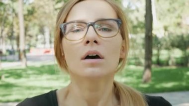 Gözlüklü genç beyaz kadın alerjisi olan parkta ayakta burun üfleme. Hasta kız hapşırma ve ağaç polen alerjisi nedeniyle doku içine burnunu üfleme.
