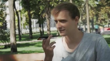 Mutlu adam bir akıllı telefon ses tanıma ses tanıma ses ai mesaj konuşma fonksiyonu kullanarak hat şehir arka plan ile bir sokakta yürüyüş, konuşma mesajı yardımcı öğrenci erkek bankta parkta 