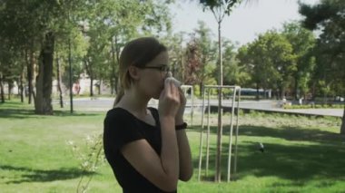 gözlük genç hasta kadın yaz günü bir şehir parkında hapşırma yürüyüş