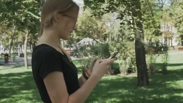 스마트 프로그램을 사용하여 아름다운 여성의 초상화 미소와 전화에 메시지 공원에서 — 비디오