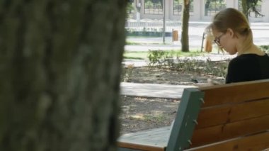 Mutlu kız öğrenci bir şehir parkında bir bankta oturan bir akıllı telefon kullanarak, genç kadın gülümseyen kullanım uygulaması, uzun sarı saçlı. 