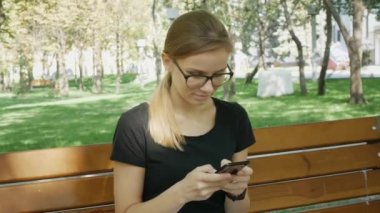 Gözlüklü Kadın Cep Telefonu yla Sohbet Ediyor.Rahat Kız Oturve Şehir Parkı'nda Cep Telefonuna Bakıyor. Akıllı Telefon Outdoors.Woman Kullanarak Sohbet Olan Güzel Kadın Arkadaşı ile Sohbet. 
