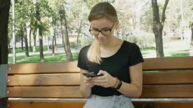 Gözlüklü Kadın Cep Telefonu yla Sohbet Ediyor.Rahat Kız Oturve Şehir Parkı'nda Cep Telefonuna Bakıyor. Akıllı Telefon Outdoors.Woman Kullanarak Sohbet Olan Güzel Kadın Arkadaşı ile Sohbet. 