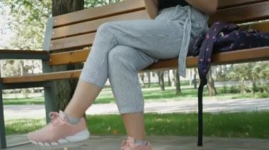 Gözlüklü beyaz kadın siyah cep telefonu kullanıyor ve şehir parkında bankta oturuyor