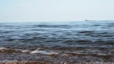 Kumlu plajda deniz dalgalarının görüntüleri kapatın. Odaklanmış bir gemi arka planda yüzüyor. Sakin yaz akşamı.