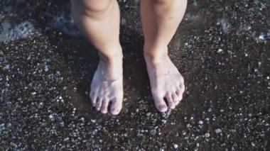 Kadının bacakları gün batımında deniz suyuna küçük atlar yapar. Yakın çekim, plajda deniz suyuna atlayan kadın bacakları, tatil konsepti. 