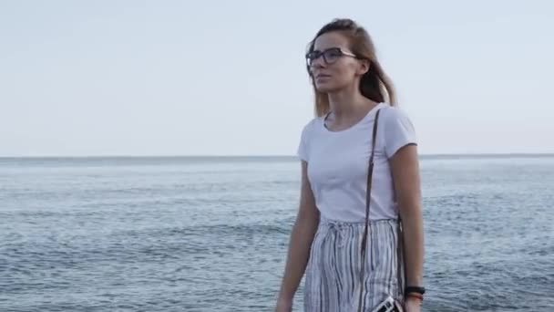 年轻的美丽的女人穿着白色短裤走在海边与旧的复古相机在夕阳的背景 特写无忧无虑的女性在沙滩上享受大自然和阳光 — 图库视频影像