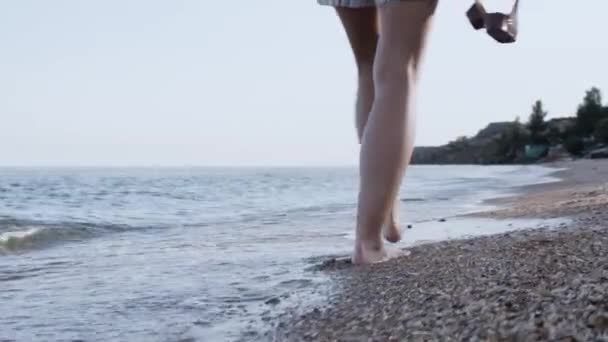 Krásná scéna ženské fotografa se starou kamerou, která při západu slunce kráčí po mořské pláži. Při chůzi na pláži se rozstřílila stopa po ženských nohách.