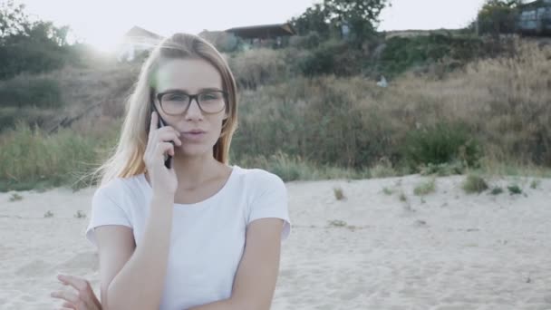 夏には海のビーチで海を見て 電話を話す女性観光客 白いTシャツとショートパンツを着た肖像画の白人モデル — ストック動画