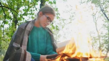 Yürüyüşçü kız kamp ateşinin yanında kitap okuyor. Sağlıklı, aktif yaşam tarzı olan insanlar. 