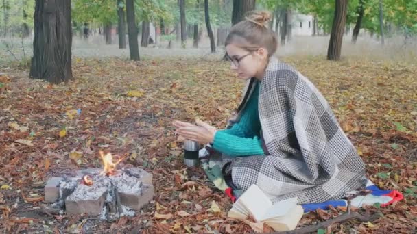 秋の前夜に火のそばに座っている暖かい緑のセーターの若い白人女性 — ストック動画