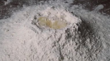 Un stokuna yumurta düşmesi. Görüntülü yemek. Un içine yumurta düşmesi, ağır çekim. Yumurta sarısı unun içine düşer. Yemek bloğu, un ürünleri. Fırın ürünleri. Hamurun hazırlanması
