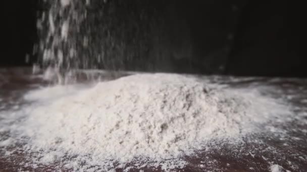La farine tombe sur la table noire au ralenti. Quelqu'un jetant de la farine sur un fond sombre. Mouvement lent de la farine blanche tombant sur le fond noir.