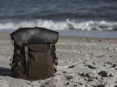Hipster hiker tourister khaki backpack close up on background blue sea ocean horizon on sand beach, blurred panoramic seascape blank, traveler relax holiday concept, sunlight view in trip vacation clipart