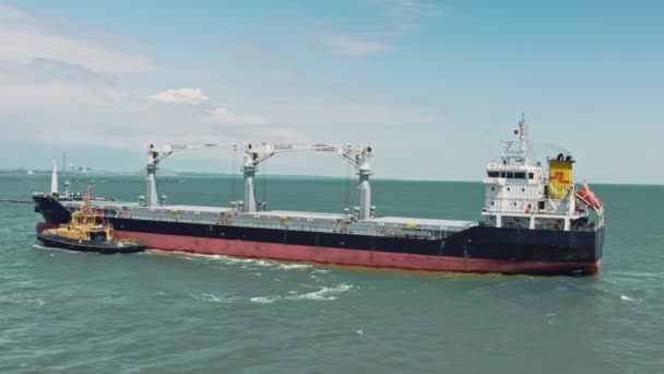 Εναέρια drone βίντεο του πλοίου μεταφοράς εμπορευματοκιβωτίων καθοδηγείται από κίτρινο ρυμουλκό βοηθητικό σκάφος στο εμπορικό λιμάνι logistics. Το ρυμουλκό μεταφέρει ένα μεγάλο πλοίο στην αποβάθρα του λιμανιού. — Αρχείο Βίντεο