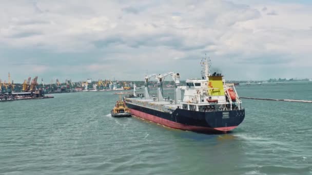 Flygdrönare video av last container fartyg styrs av gula bogserbåt hjälpmedelbåt till logistik kommersiell hamn. Bogserbåt transporterar ett stort fartyg till hamnen. — Stockvideo