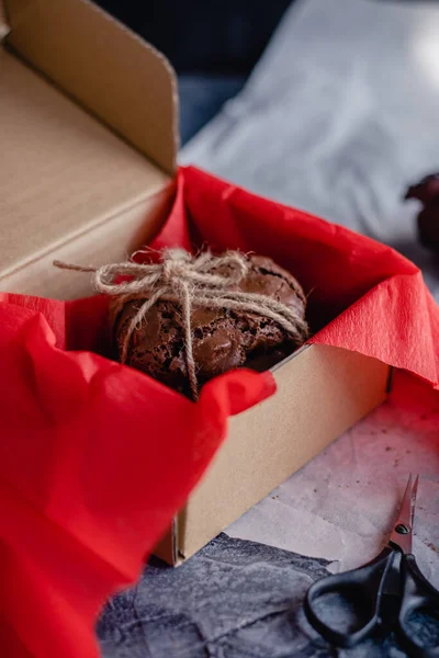 Homemade chocolate chip cookies on red paper in a craft cardboard box on a dark background. DIY gift.