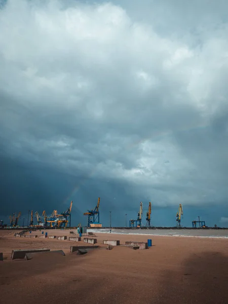 Port cranes under the dark clouds after the thunderstorm. Dramatic stormy sky. Industrial landscape. Idle cranes in front of storm clouds