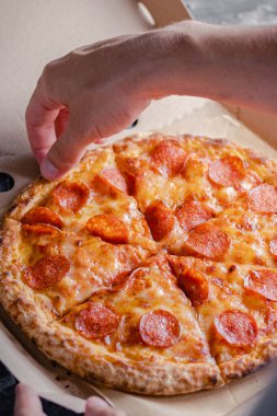 Erkek el, pepperoni pizzasının ilk dilimini teslimat kutusundan çıkarır. Fast food konsepti.